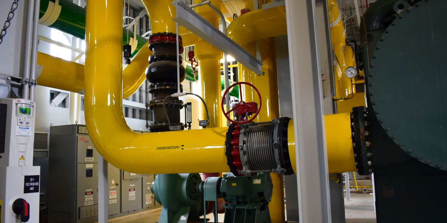 Large yellow ground-source heat pump condenser piping at a campus geothermal system
