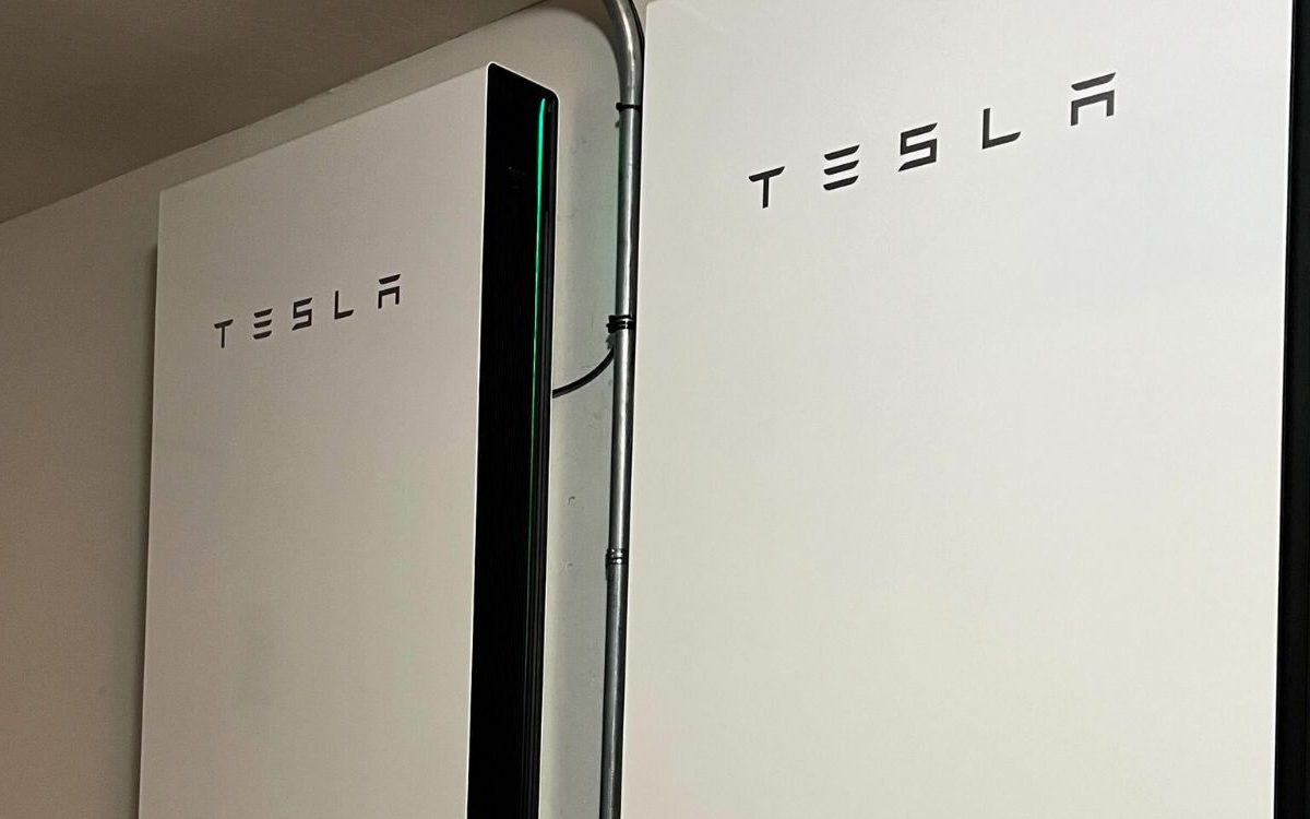 Two Tesla Powerwall 3 home batteries mounted on a garage wall with a disconnect box