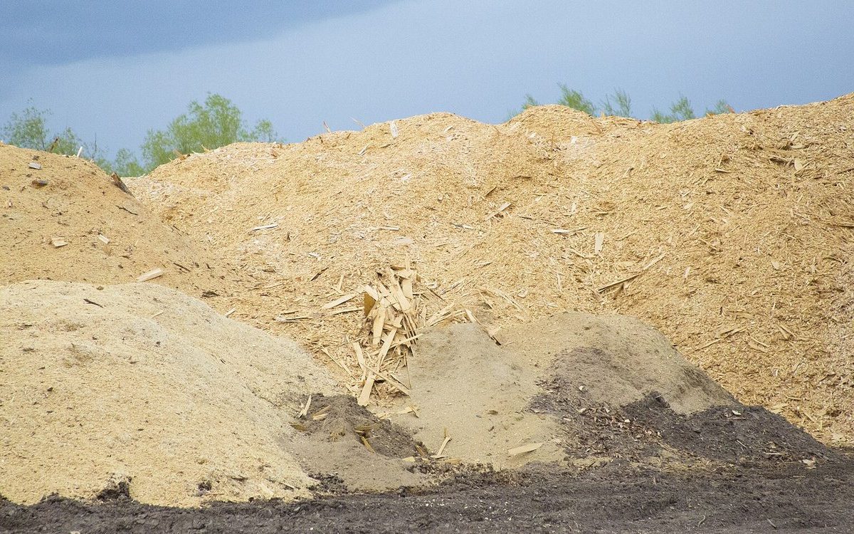 Large piles of wood chips at an outdoor yard under a cloudy sky
