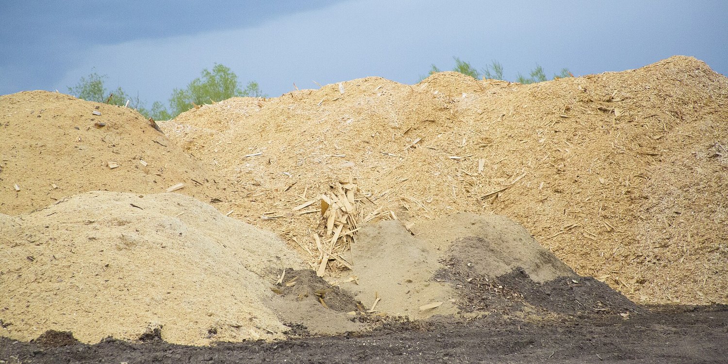 Large piles of wood chips at an outdoor yard under a cloudy sky