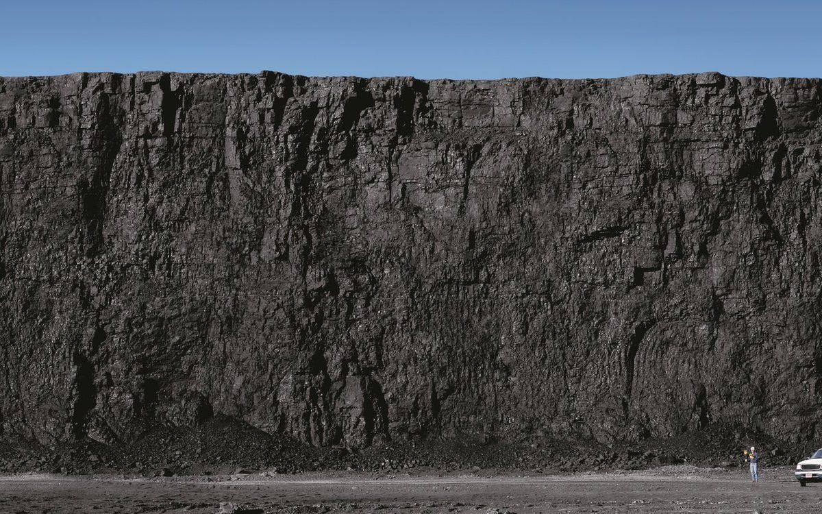 A thick coal seam exposed in the wall of a surface coal mine, with a truck at its base for scale