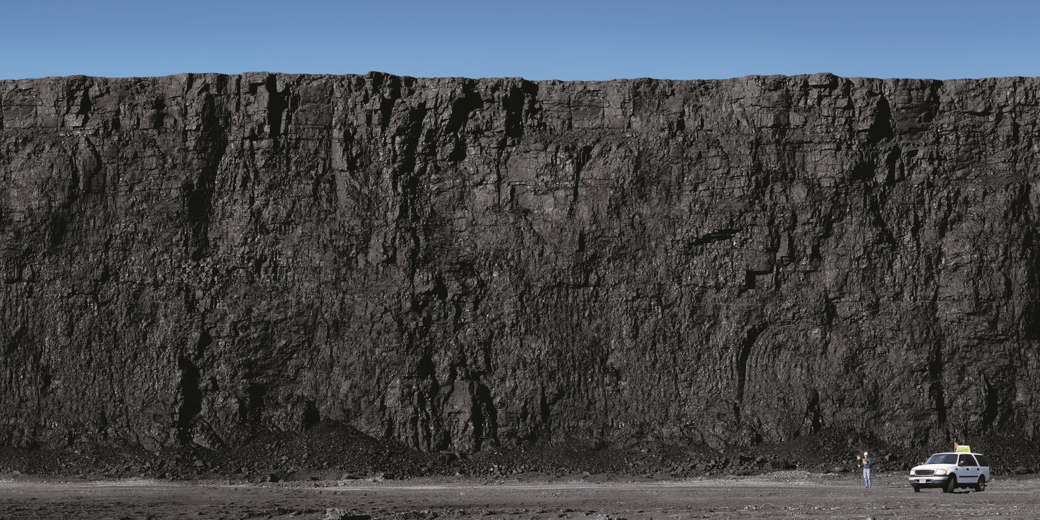 A thick coal seam exposed in the wall of a surface coal mine, with a truck at its base for scale