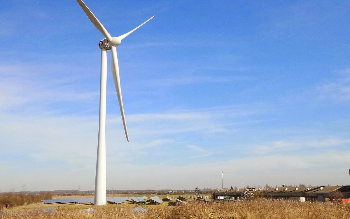 A wind turbine standing beside rows of solar panels on open farmland