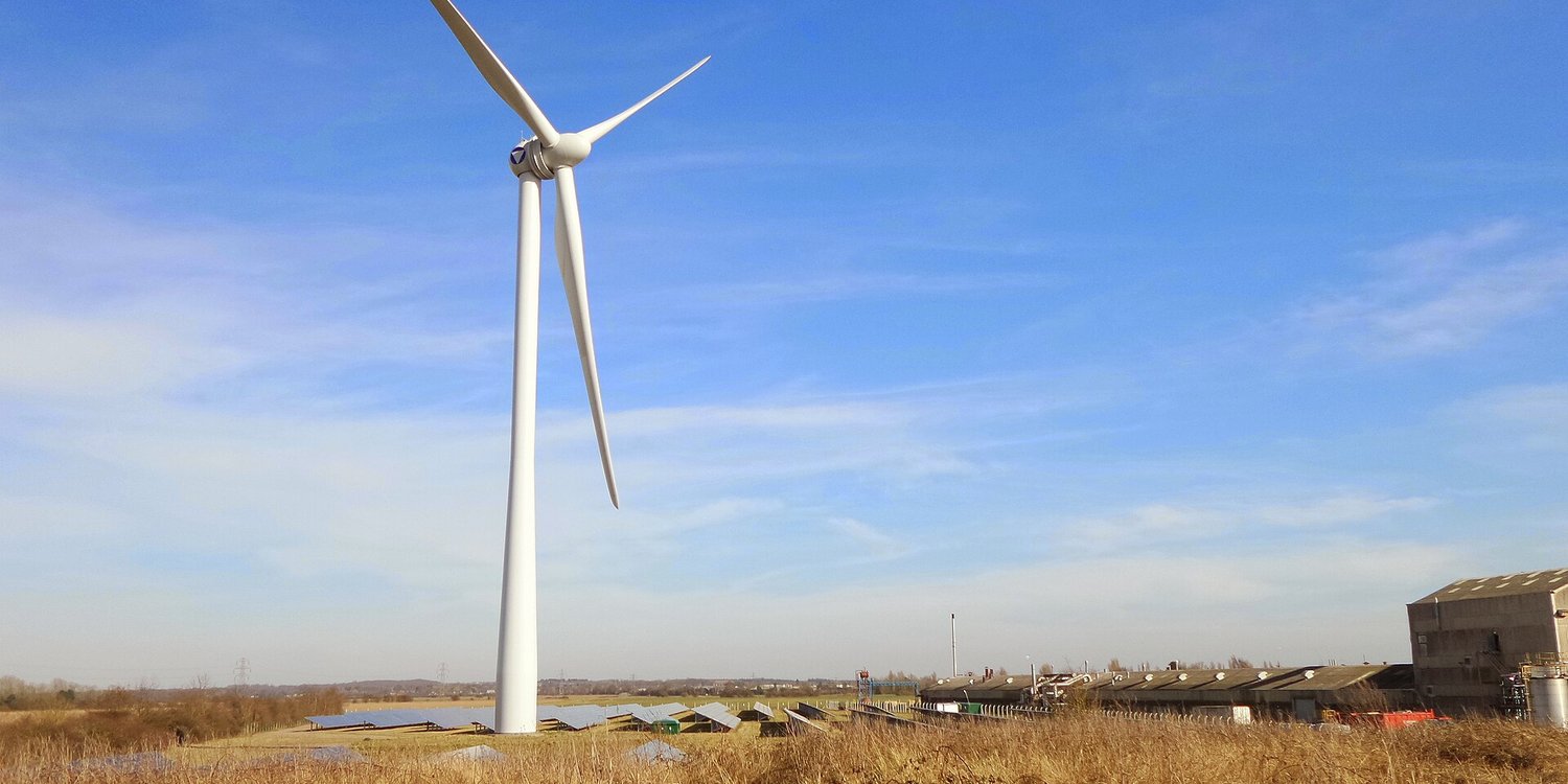 A wind turbine standing beside rows of solar panels on open farmland