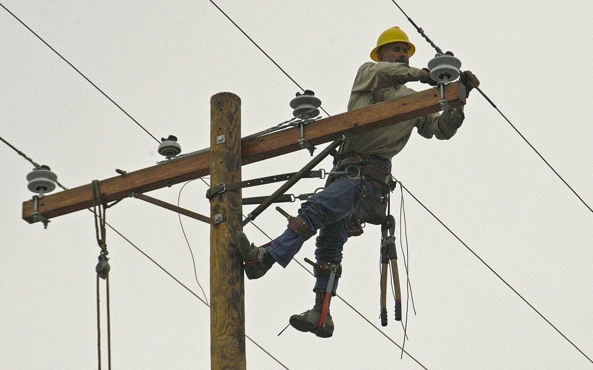 A utility lineworker repairing a power line from the top of a pole