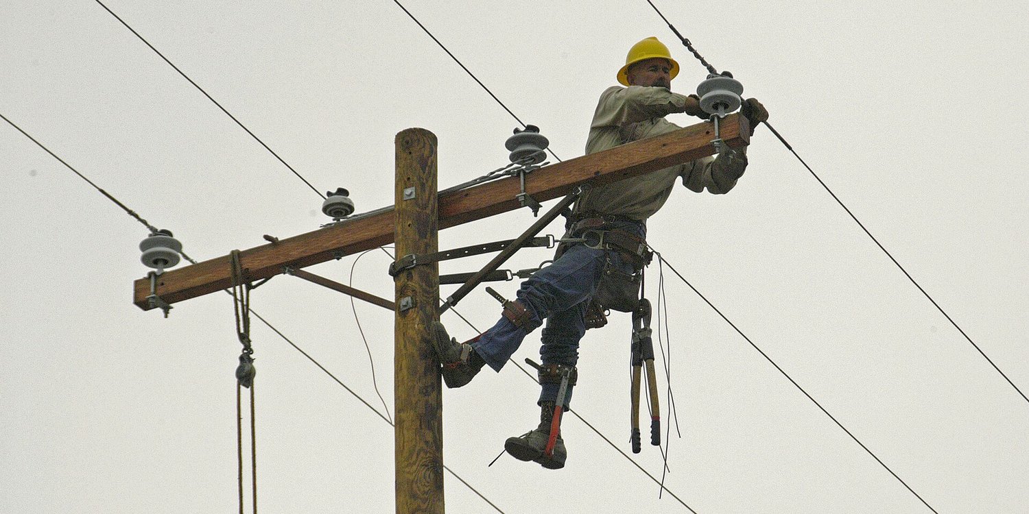 A utility lineworker repairing a power line from the top of a pole